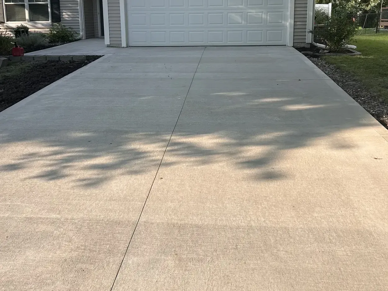 Finished replacement concrete driveway at a Waukee, Iowa home, backfilled and edged, running from the street up to the garage.