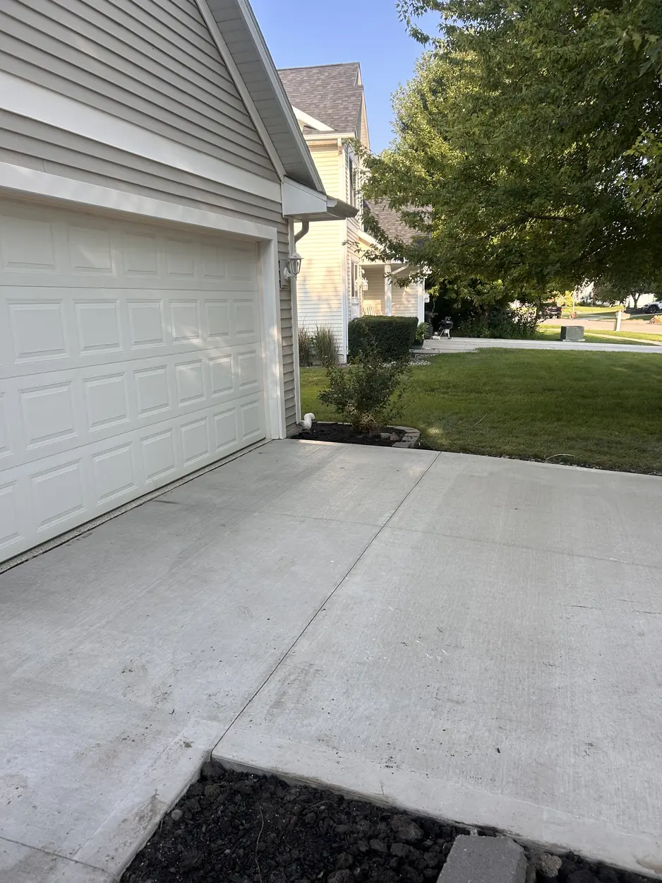 Replacement concrete driveway at a Waukee, Iowa home seen from the garage side, backfilled and edged, running out toward the street.