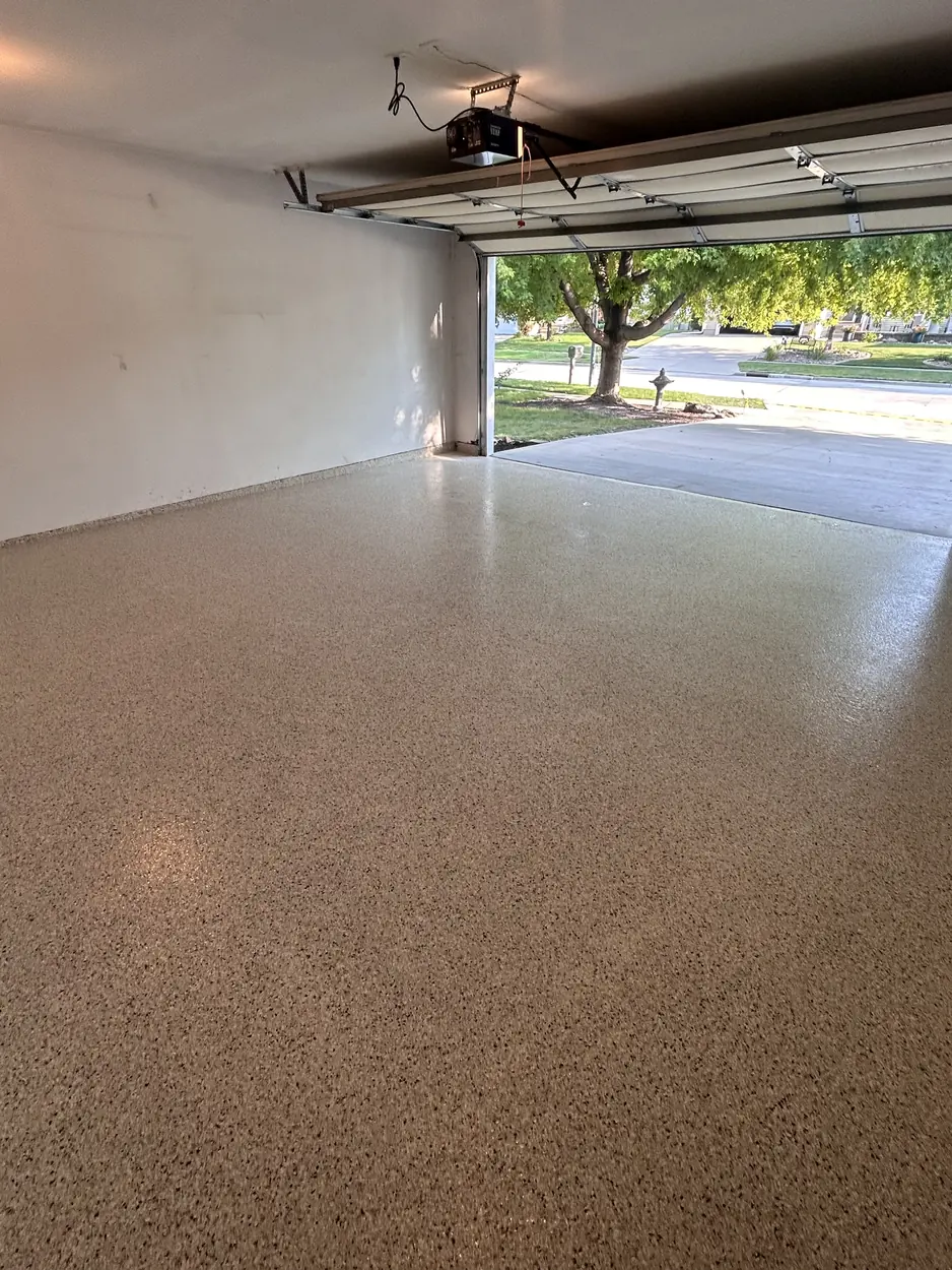 The same Waukee, Iowa garage floor finished with an epoxy base coat, flake broadcast and polyaspartic clear topcoat, photographed from the same corner as the prep shot.